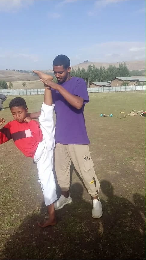 Instructor supporting a young student's raised leg during outdoor training