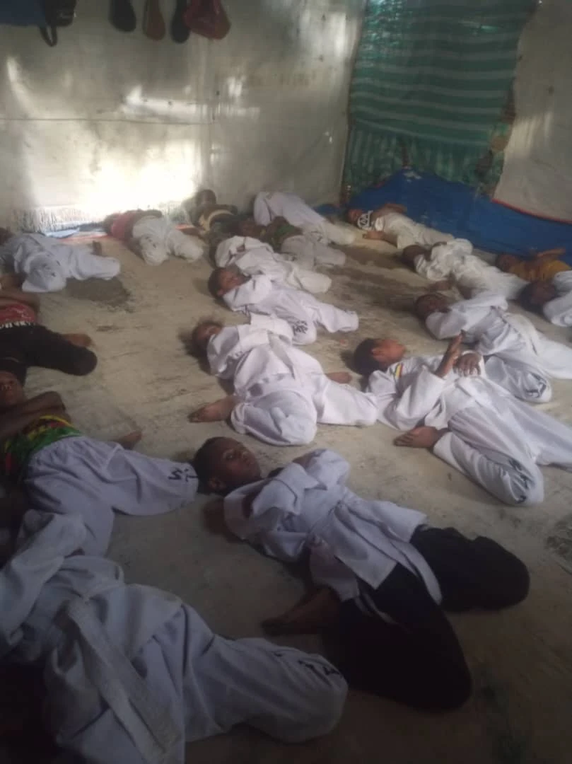 Group of participants in white martial arts uniforms lying in rows across an indoor training-room floor